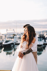 Happy lovers, the bride and groom in elegant wedding dresses go on a honeymoon by sea on  yacht in...
