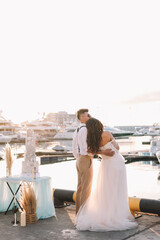 Happy lovers, the bride and groom in elegant wedding dresses go on a honeymoon by sea on  yacht in...
