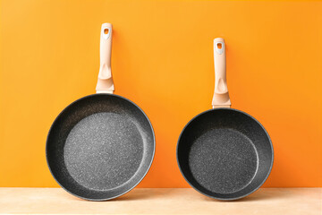 Copper frying pans on table against orange background