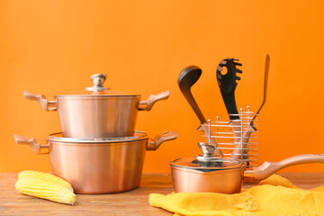 Copper kitchen utensils and raw food on table against orange background