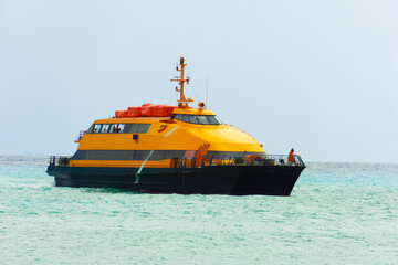 An orange ferry sails across the sea on a cloudy day. Small figures of sailors on the deck of the yacht. Ship on the water.