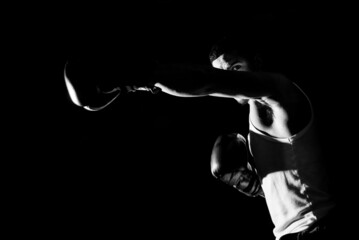 Young man practicing shadow boxing over black background. Black and white high contrast image....