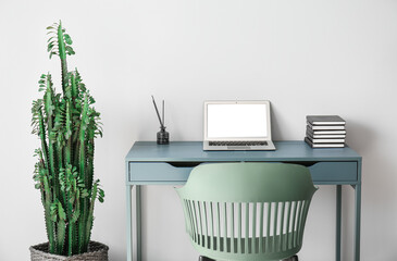 Modern workplace with laptop and big cactus near light wall