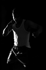 Fototapeta na wymiar Young man practicing shadow boxing over black background. Black and white high contrast image. Strenght and motivation.