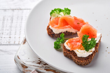 Mini sandwiches with salmon, curd cheese, parsley and rye bread in form of hearts. Valentine's day homemade creative food. Love breakfast design. Selective focus and copy space