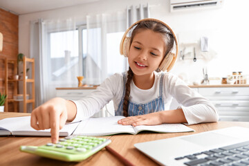 Little girl in headphones studying Math with online tutor at home