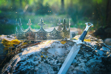 mysterious and magical photo of silver king crown and sword over stone in the England woods....