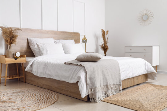 Comfortable bed, dry reeds and chest of drawers near white wall