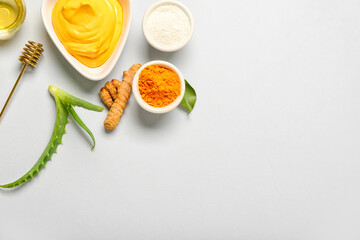 Bowl with turmeric mask, powder and aloe on grey background