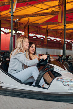 Two young women drive a bumper car while they are smiling