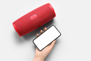 Female hand with mobile phone and wireless portable speaker on light background