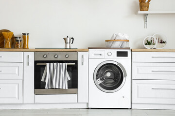 Interior of light kitchen with washing machine, oven and white counters