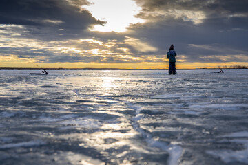 A young boy ice fishing on a frozen lake with a dramatic sky reflection in Alberta Canada