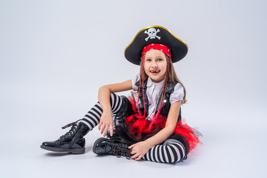 Portrait of a naughty little girl in a pirate costume, sitting on a whrite background, A girl is preparing for the Halloween holiday.