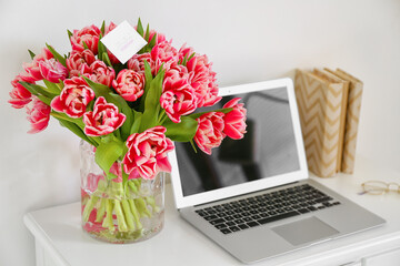 Workplace with modern laptop and bouquet of beautiful tulips near light wall. International Women's Day celebration