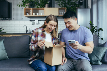 Family at home happy sitting on the couch, received a parcel from the online store, multiracial couple at home, man and woman together