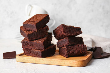 Wooden board with pieces of delicious chocolate brownie on light background