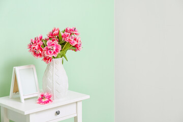 Vase with beautiful tulips and blank photo frame near color wall. International Woman's Day celebration
