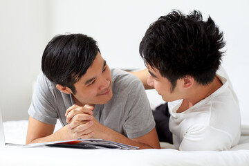 Living and loving together. Cute young gay Asian couple smiling while relaxing at home together.
