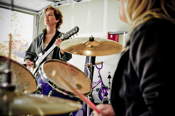 View over drummers shoulder of guitar player in Garage band composed of middle aged women, practicing in residential garage 