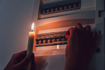 Energy crisis. Hand in complete darkness holding a candle to investigate a home fuse box during a...