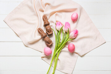 Composition with chocolate Easter bunnies, eggs and tulip flowers on light wooden background