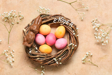 Nest with colorful Easter eggs, chocolate bunny and gypsophila flowers on color background
