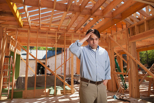 Man hand on his head looking down in worry at a residential construction site