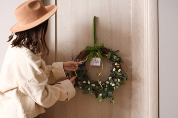 Young woman hanging Easter wreath on wooden door