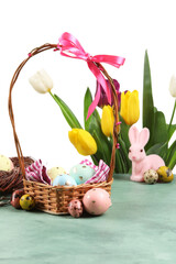 Obraz premium Basket with painted Easter eggs and tulip flowers on table against white background