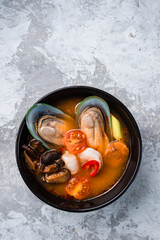 Traditional spicy Thai soup Tom Yum with shrimp and seafood in ceramic bowl on stone background