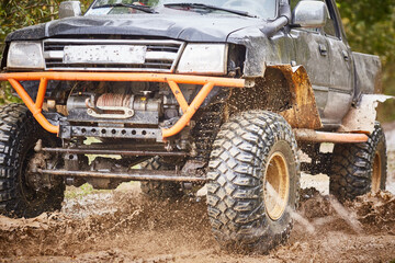 Traveling off-road on dirty off-road on a black and orange truck. Close-up of the wheel, suspension in a puddle and mud