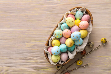 Basket with painted Easter eggs and willow branches on wooden background