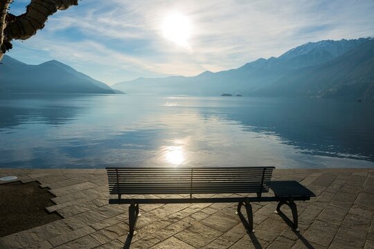 Bench on the Waterfront on Alpine Lake Maggiore with Sunlight and Mountain in Ascona, Switzerland.