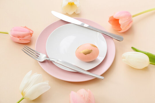 Beautiful table setting with Easter egg and tulips on beige background