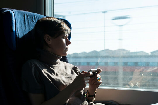 Woman 21 in a Train with Sunlight and Using Smartphone in Milan, Italy.