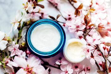 Obraz na płótnie Canvas Skincare lotion and eye contour product. Herbal spa cosmetic cream with pink cherry flowers in a blue glass jar.