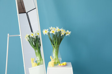 Vase with daffodils flowers, Easter decor on table and mirror near color wall