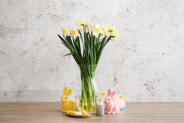 Vase with flowers, Easter eggs and bunnies on wooden table near grunge wall