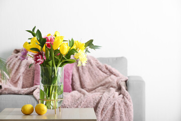 Vase with tulips and lemons on table in light living room