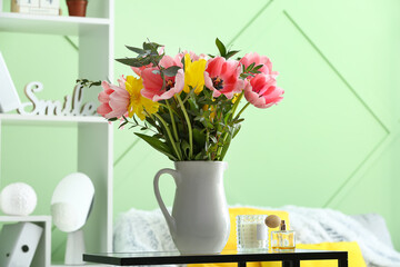 Vase with tulips, perfume and candle on table in living room