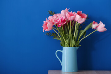 Vase with pink tulips on table near blue wall
