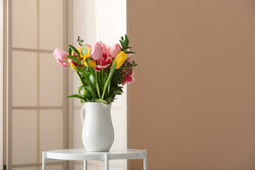 Vase with spring flowers on table and folding screen near beige wall