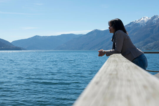 Woman Standing and Leaning on a Railing on the Waterfront to an Alpine Lake Maggiore with Mountain in Ascona, Switzerland.