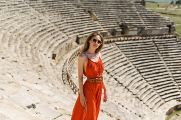 A young beautiful woman in a red dress walking in Pamukkale, Turkey, against the backdrop of the...
