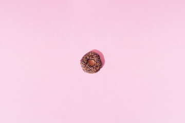 Ring donuts with chocolate glaze and small crumbs on a pink pastel background. Minimal design and pattern.