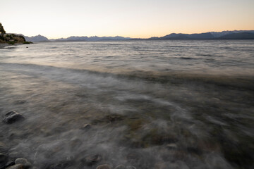 Long exposure shot of Nahuel Huapi lake at sunset. Beautiful blurred water effect, the rocky shore, waves and dusk colors .