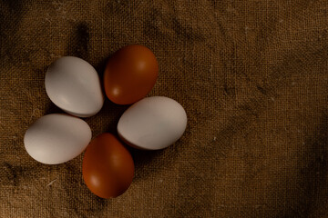 Five eggs with white and brown shells, lying around, on textured burlap. Easter Eve, white and brown eggs, on a substrate with an unusual texture.