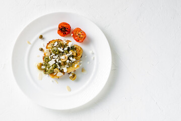 Cauliflower steak with spices, chimichurri sauce, almond flakes, olives, fried cherry tomatoes and capers on a white plate. Vegetarian food.