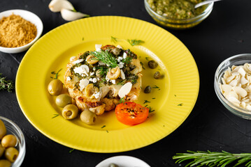 Baked cauliflower steak with chimichurri sauce, almond flakes, capers on a yellow plate. Vegetarian food. Alternative delicious food.
